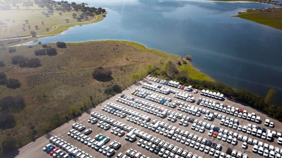 Vista aérea de un estacionamiento lleno de autos junto a una laguna rodeada de vegetación, evidenciando el contraste entre lo natural y lo construido.