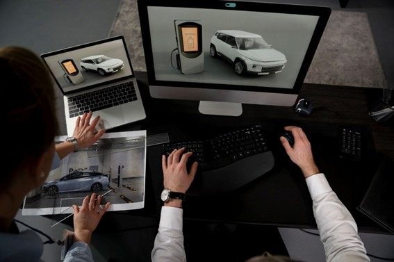 Personas trabajando en el diseño digital de un auto eléctrico con modelos 3D en pantallas y fotografía impresa del vehículo.
