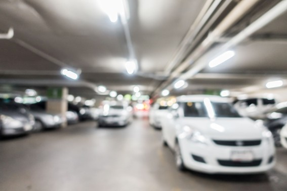 Imagen borrosa de un estacionamiento subterráneo con varios autos blancos y grises bajo luces fluorescentes.