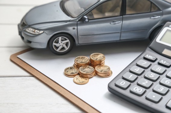 Modelo a escala de un automóvil junto a monedas apiladas y una calculadora sobre una carpeta, simbolizando cálculos de gastos vehiculares.