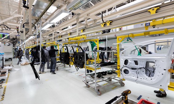 Trabajadores ensamblando puertas de autos en una línea de montaje dentro de una fábrica automotriz con estructuras mecánicas y sistema de transporte automatizado.