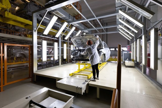 Técnica revisando un automóvil en una línea de producción bajo luces intensas en una planta de ensamblaje industrial.