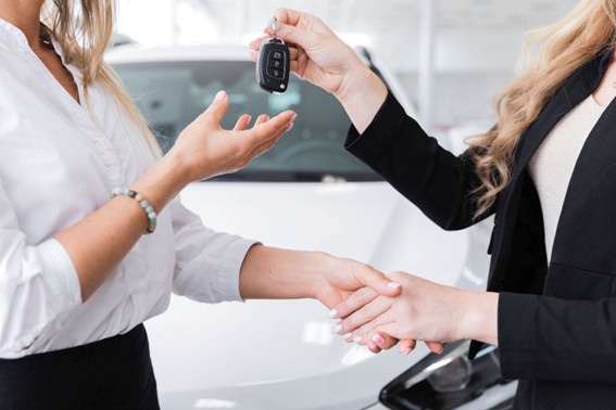 Mujer recibiendo la llave de un auto nuevo de manos de una asesora en una concesionaria.