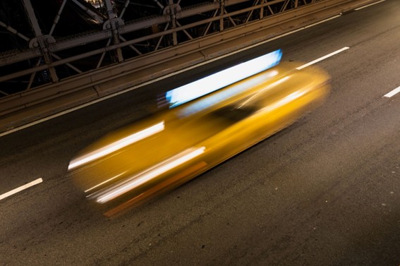 Taxi amarillo en movimiento captado con efecto de larga exposición sobre una autopista por la noche.