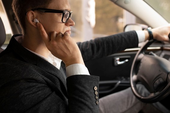 Hombre conduciendo un auto mientras usa auriculares inalámbricos y mantiene una conversación, con actitud profesional.