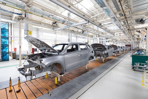 Vista de una línea de producción de autos con carrocerías sin terminar avanzando en una planta industrial automatizada.