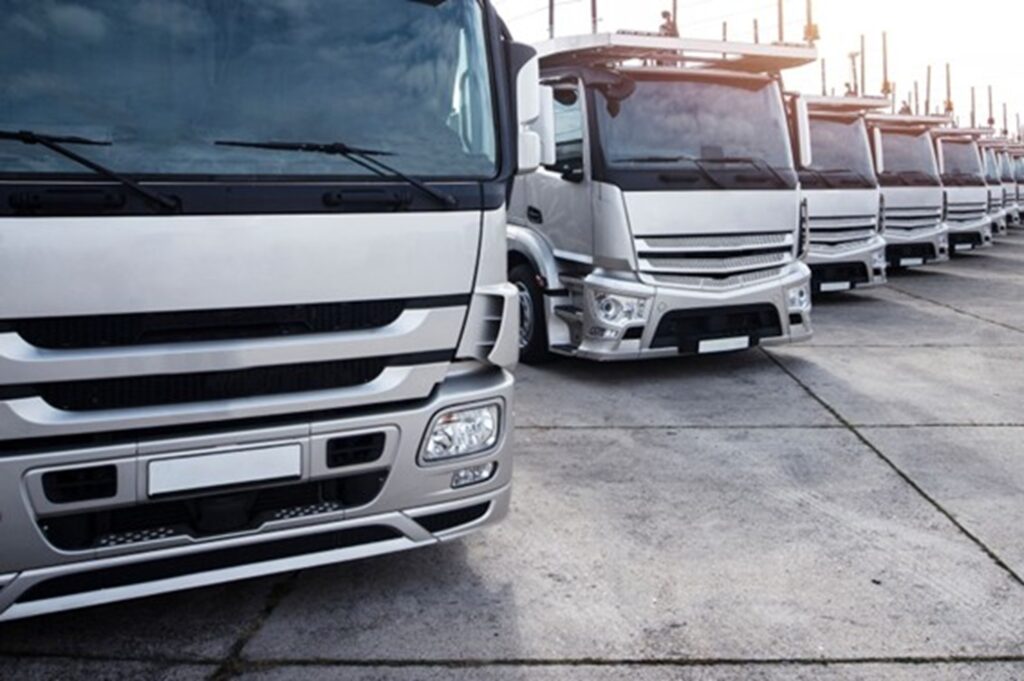 Varios camiones plateados estacionados en fila sobre una superficie de concreto, representando una flota de transporte.