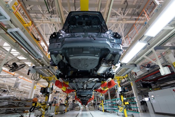 Línea de montaje con carrocerías de autos suspendidas en planta industrial.
