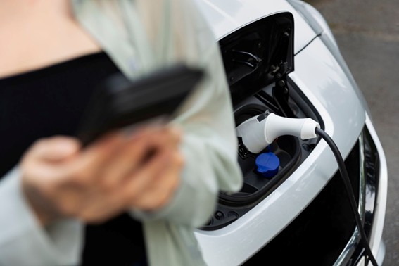 Coche eléctrico conectado a un cargador, con persona usando un dispositivo móvil en primer plano.