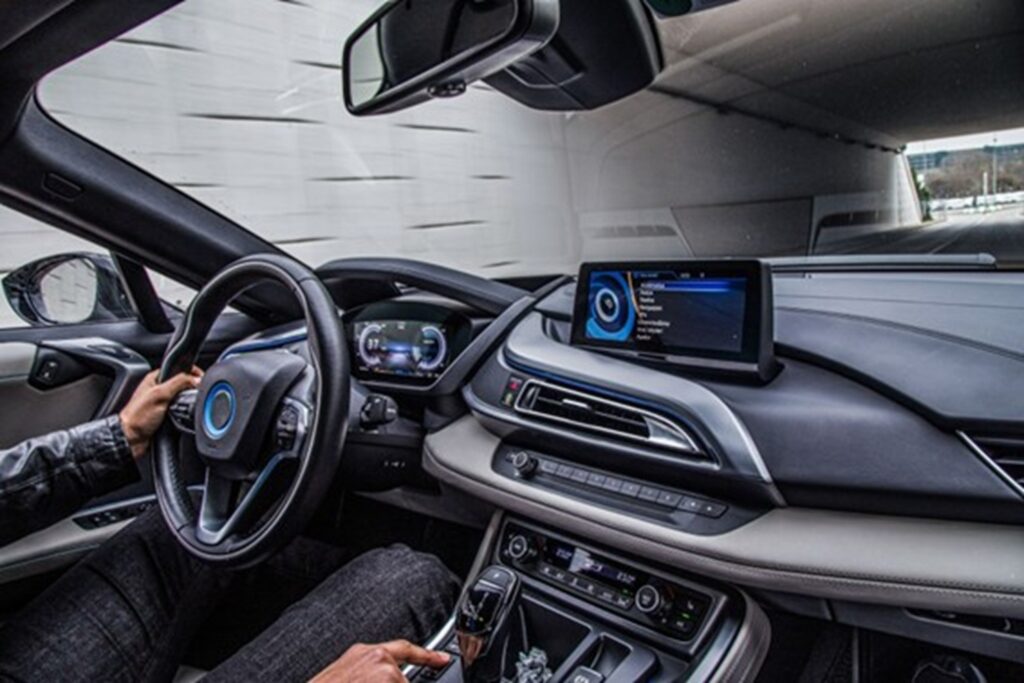 Persona conduciendo un auto moderno con volante multifunción, tablero digital y pantalla central encendida con sistema de navegación.
